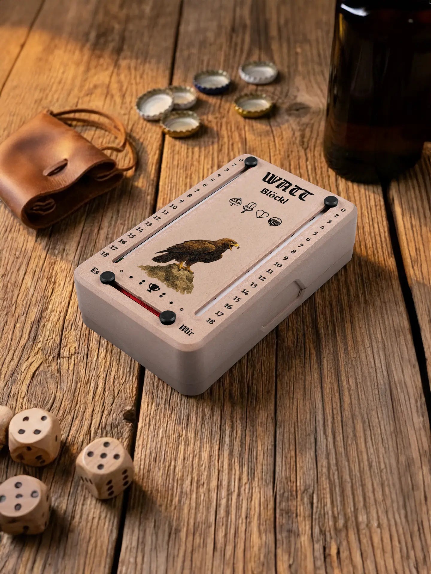 Wattblöckl in Holzoptik mit schwarzen Pins und Adler-Motiv. Platziert auf Holztisch mit Würfeln und Kronkorken.