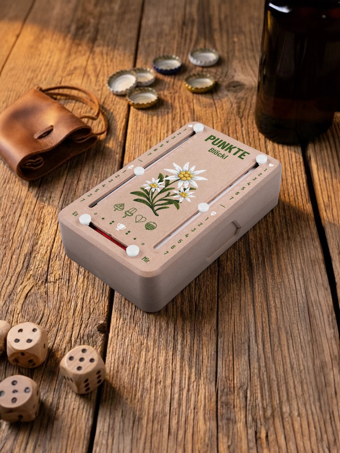 Punkteblöckl in Holzoptik mit weissen Pins und Edelweiss-Motiv. Platziert auf Holztisch mit Würfeln und Kronkorken.