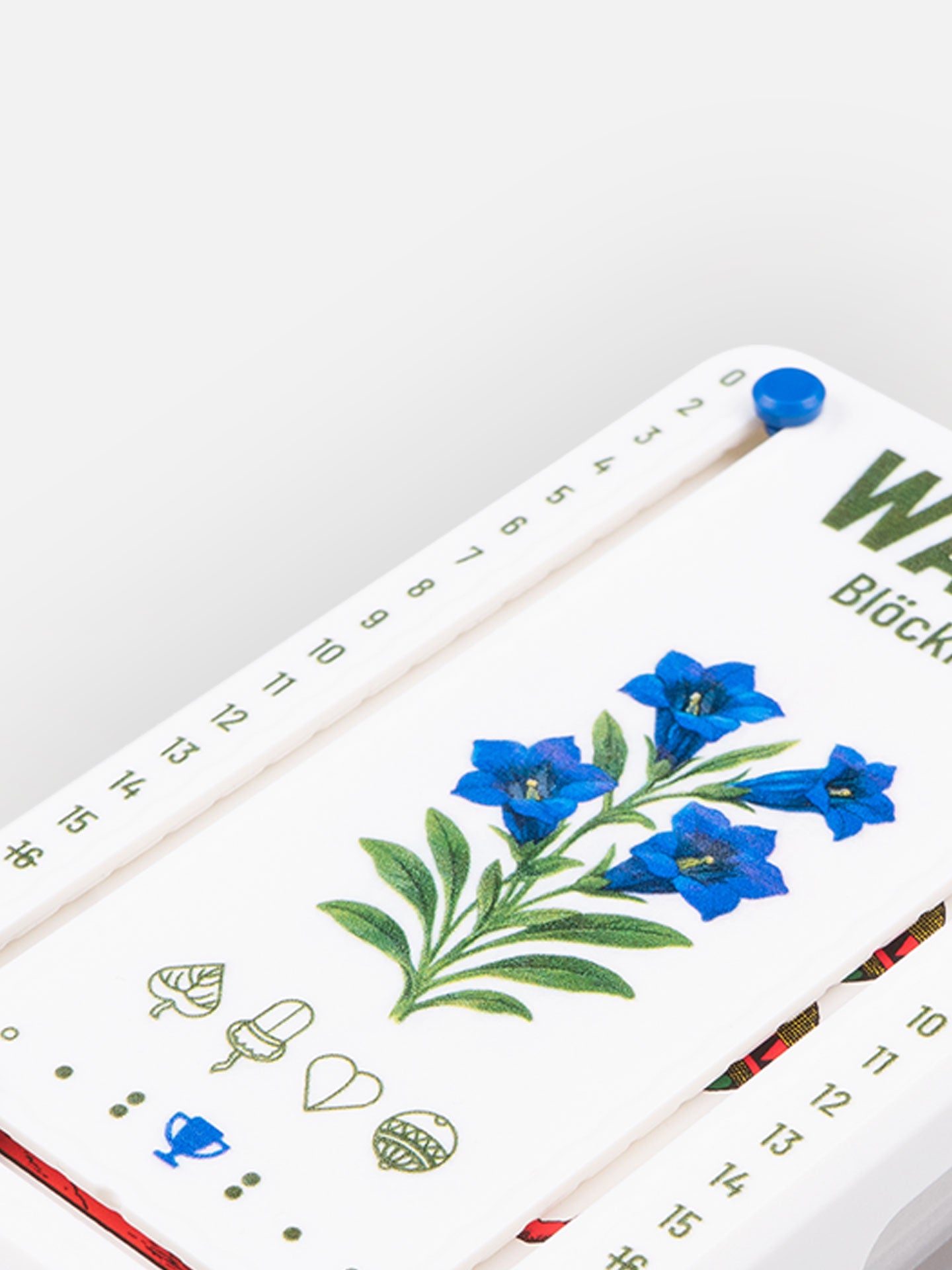 Detail Aufnahme Wattblöckl aus weißen Kunststoff mit Enzian Motiv auf grauen Hintergrund.