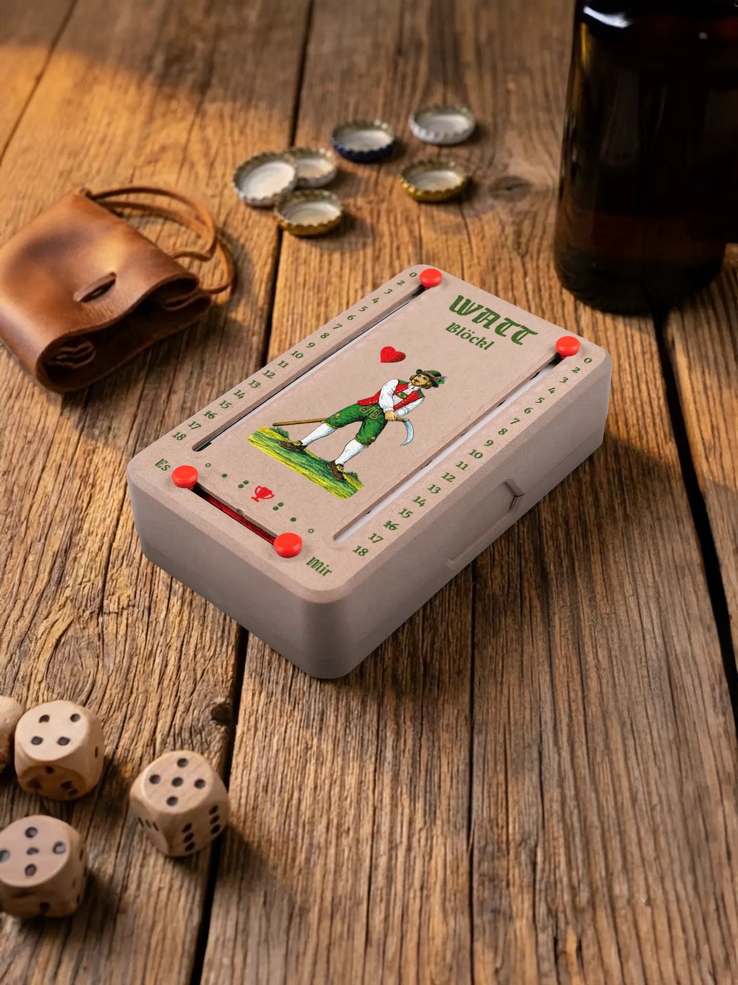 Wattblöckl in Holzoptik mit roten Pins und HerzOber-Motiv. Platziert auf Holztisch mit Würfeln und Kronkorken.