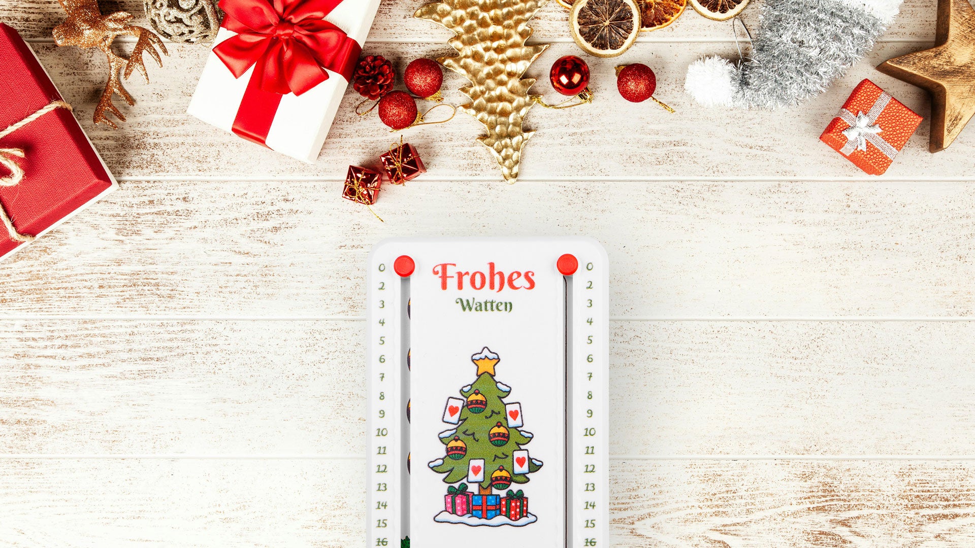 Weißes Wattblöckl mit roten Pins und Weihnachtsbaum Motiv, auf Hellen Holz- Tisch mit Weihnachtsdeko im Hintergrund