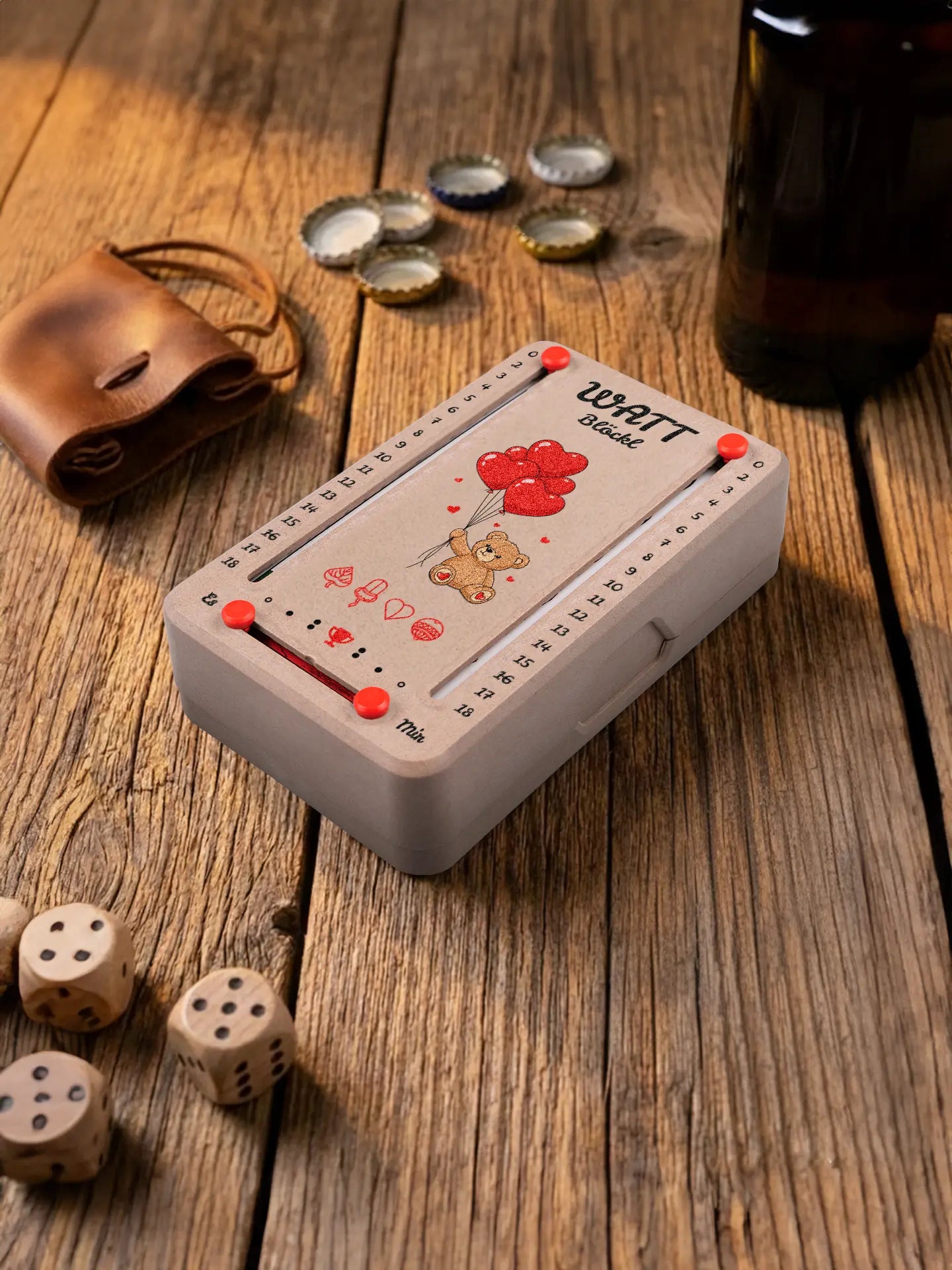 Wattblöckl  in Holzoptik mit roten Pins und Kuschelbaer-Motiv. Platziert auf Holztisch mit Würfeln und Kronkorken.