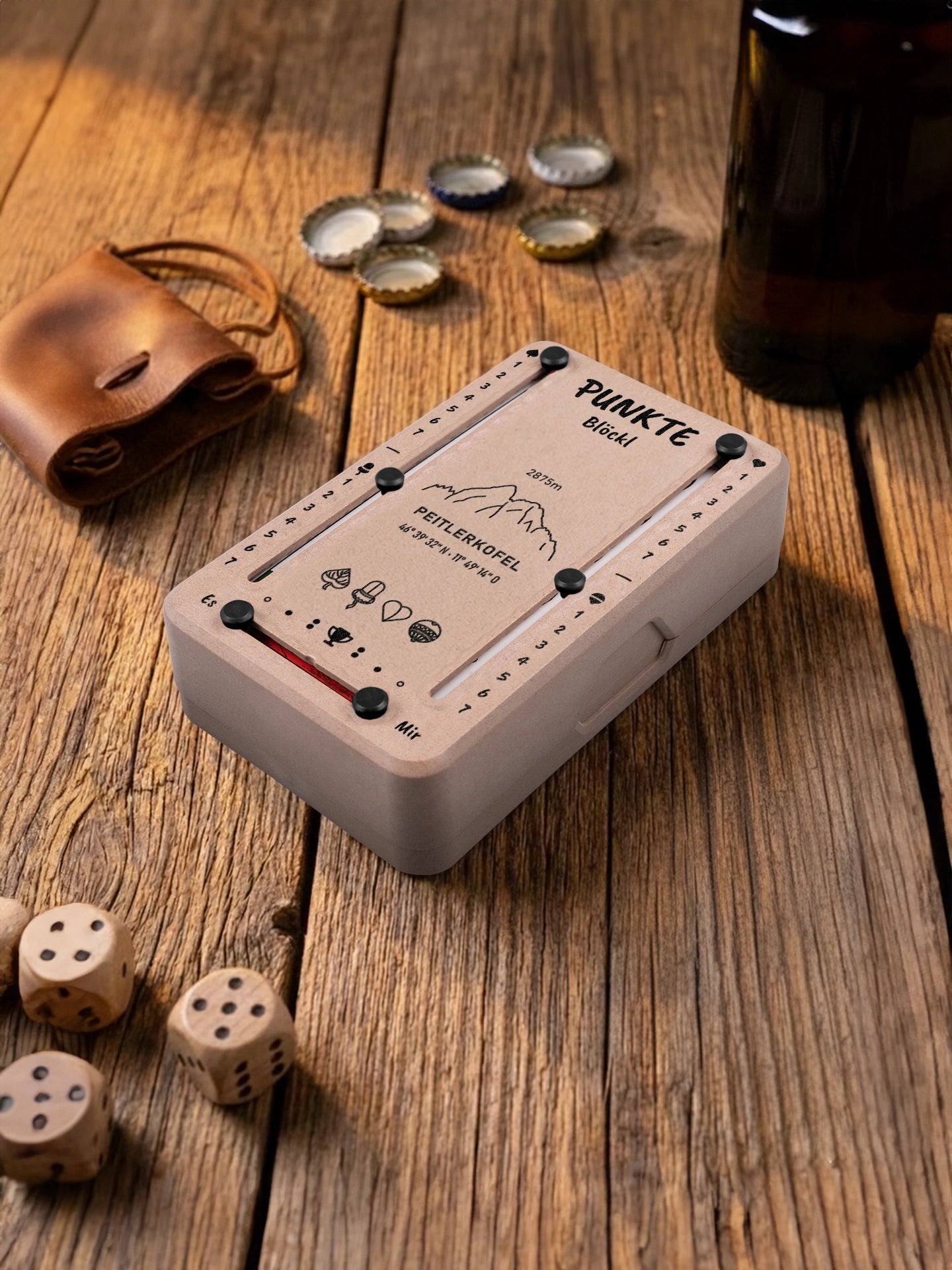 Punkteblöckl in Holzoptik mit schwarzen Pins und Peitlerkofel-Motiv. Platziert auf Holztisch mit Würfeln und Kronkorken.