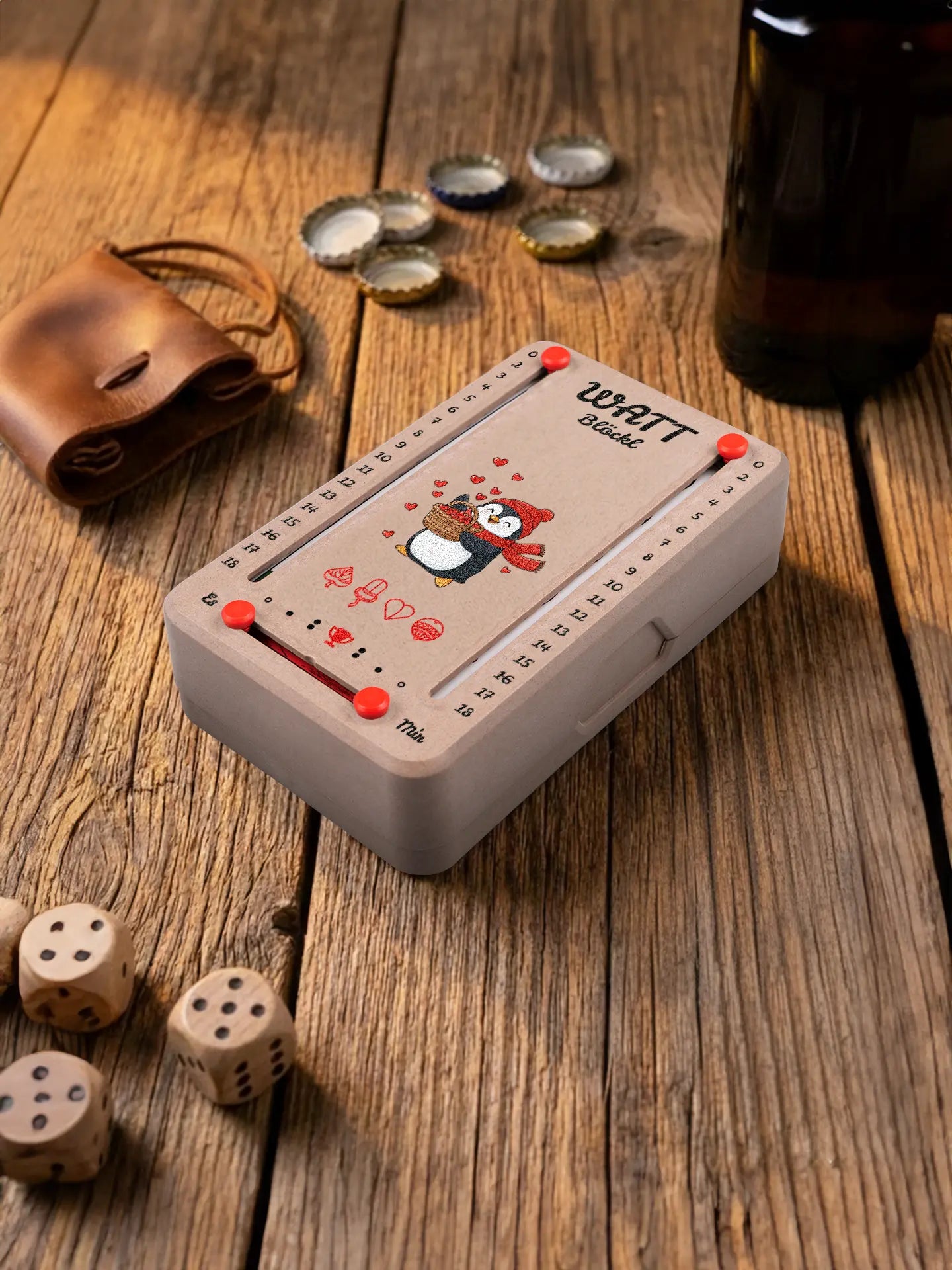 Wattblöckl  in Holzoptik mit roten Pins und Pinguin-Motiv. Platziert auf Holztisch mit Würfeln und Kronkorken.