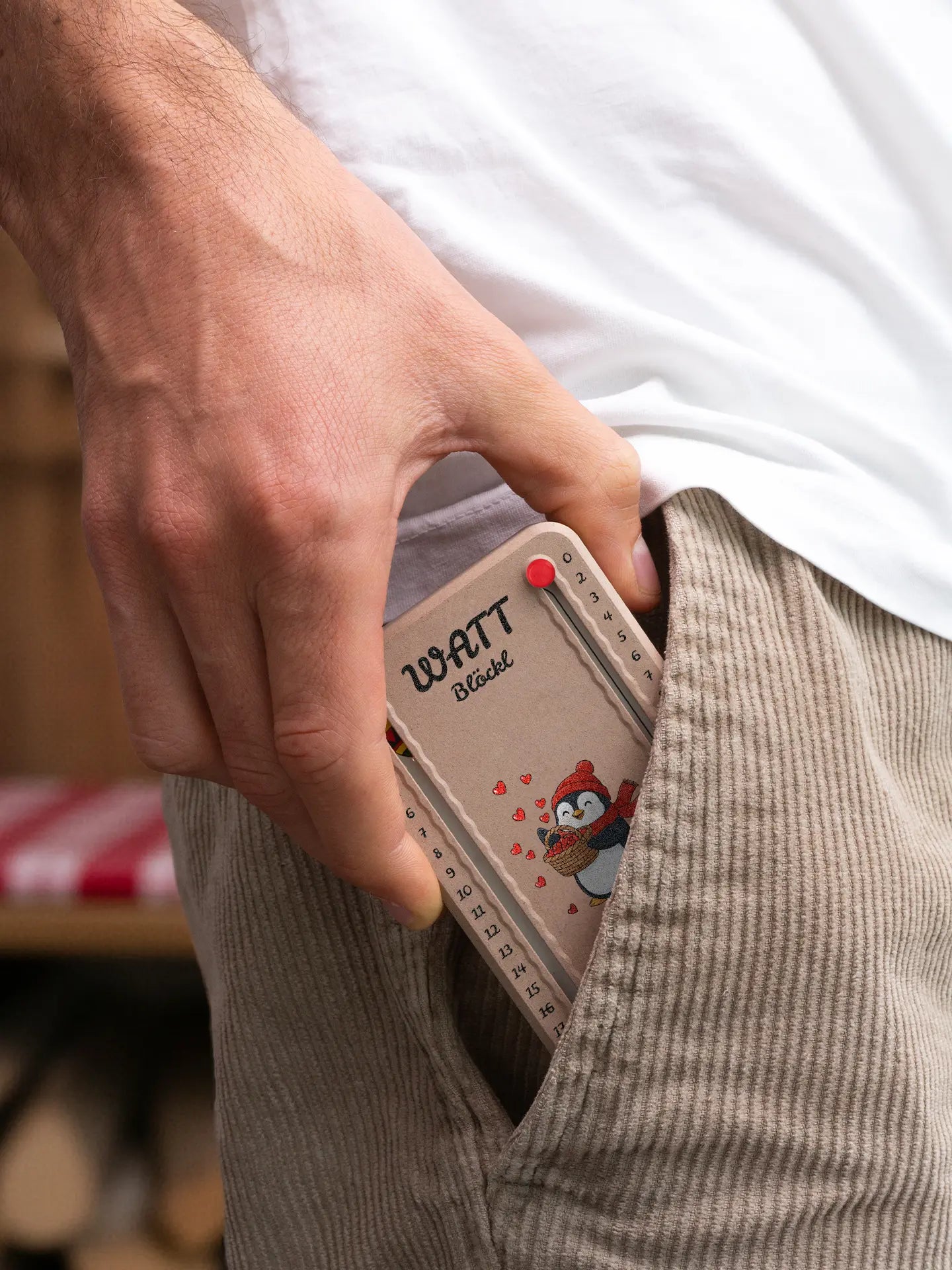 Wattblöckl in Holzoptik mit roten Pins und Pinguin-Motiv wird aus der Hosentasche gezogen.