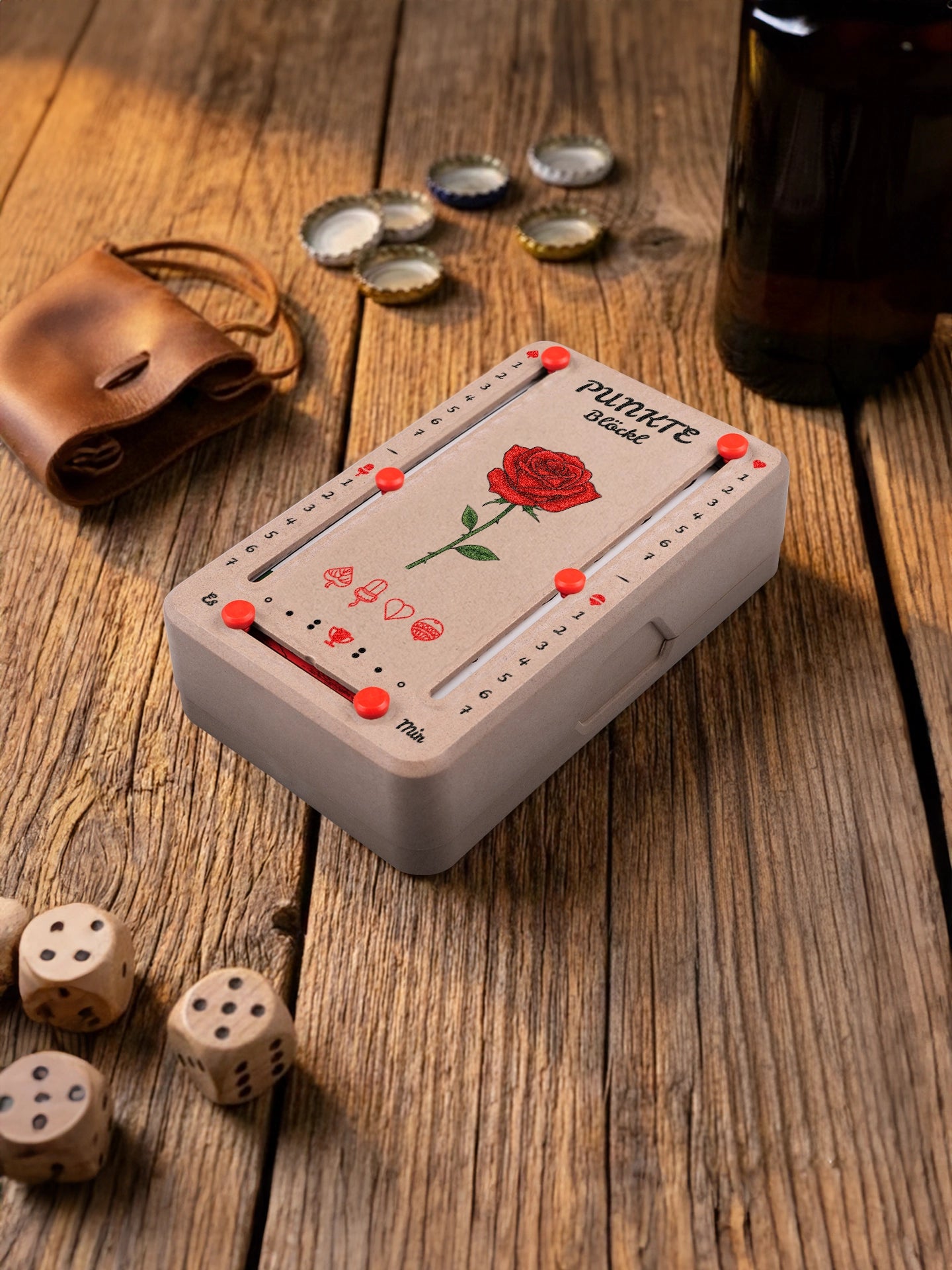 Punkteblöckl in Holzoptik mit roten Pins und Rose-Motiv. Platziert auf Holztisch mit Würfeln und Kronkorken.