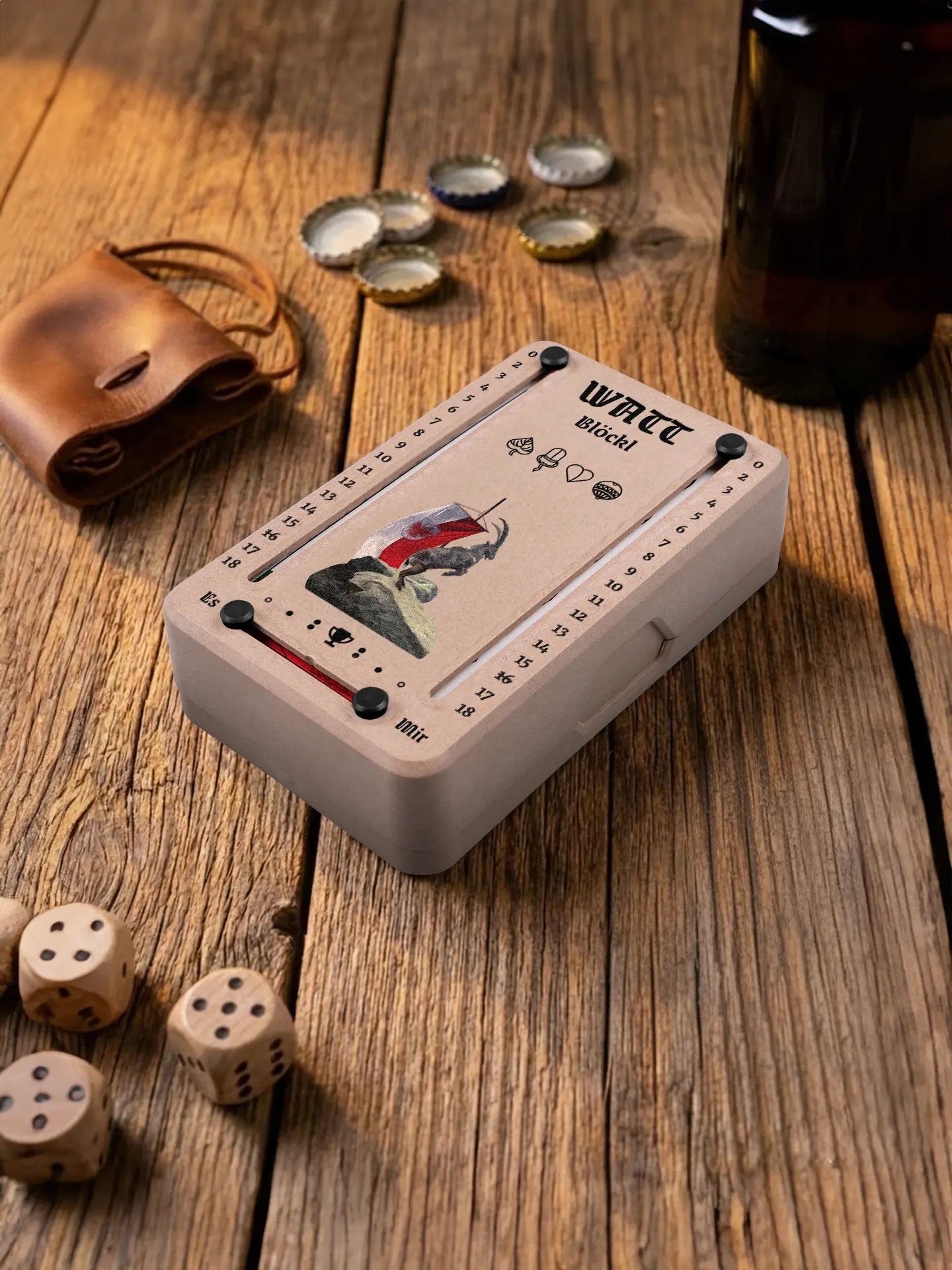 Wattblöckl in Holzoptik mit schwarzen Pins und Steinbock-Motiv. Platziert auf Holztisch mit Würfeln und Kronkorken.