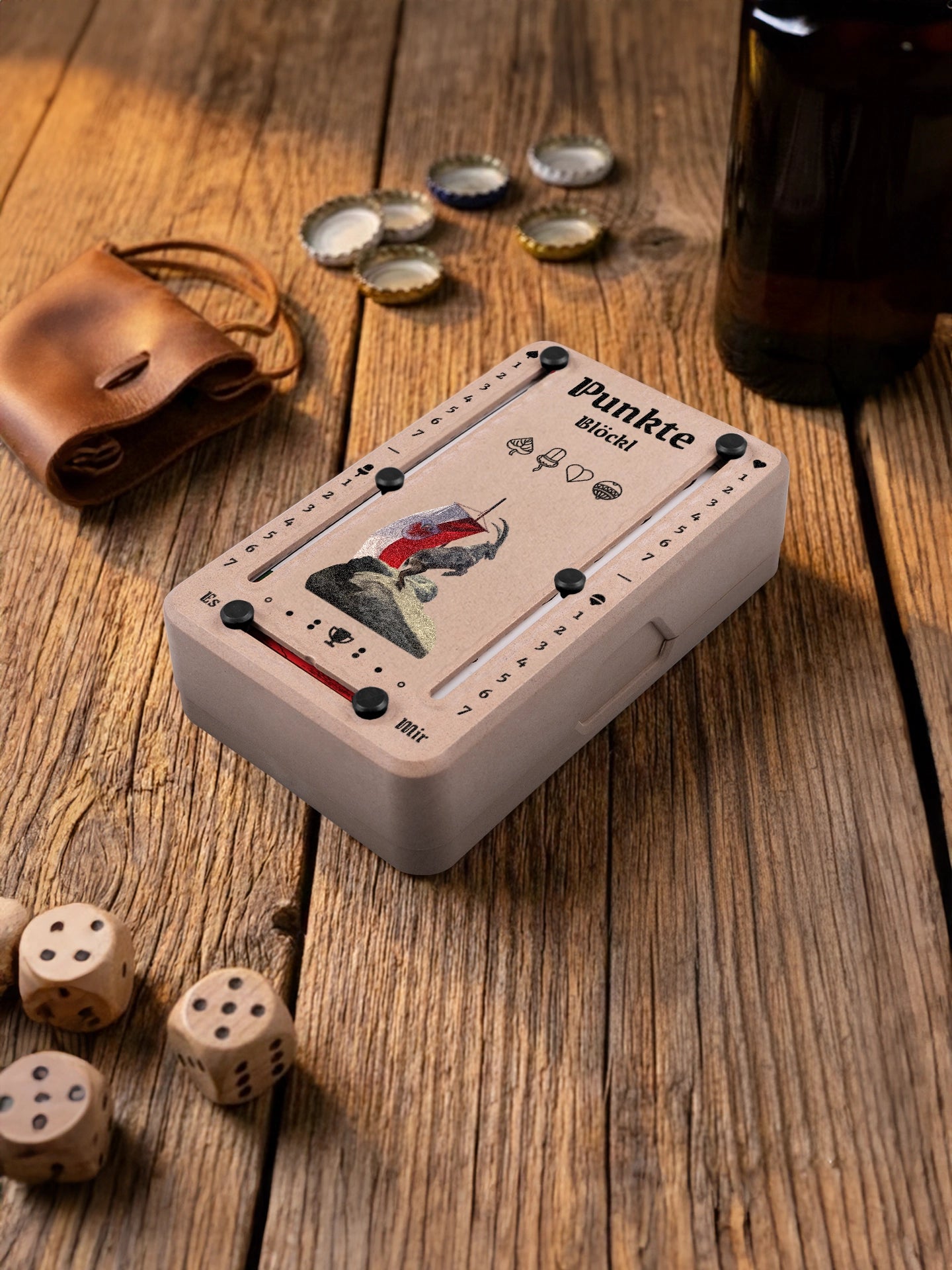 Punkteblöckl in Holzoptik mit schwarzen Pins und Steinbock-Motiv. Platziert auf Holztisch mit Würfeln und Kronkorken.